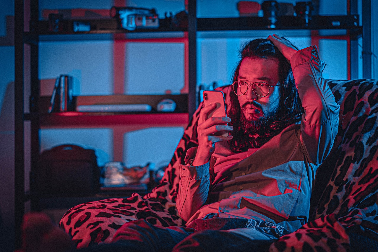 A man in a chair, looking surprised as he checks his cell phone with his right hand.