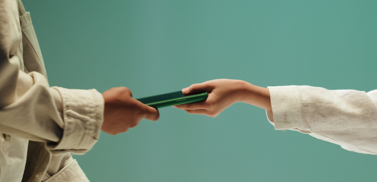 One individual hands a green phone to another, illustrating the act.