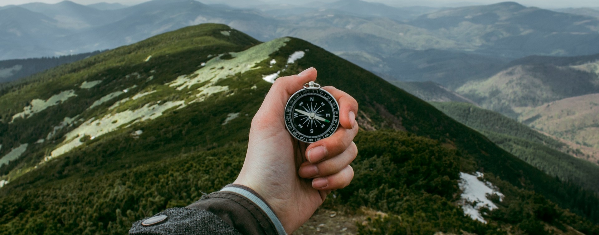 A hand holding a compass over a mountain view.